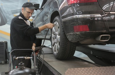 A man putting air pressure on a car tire in the garage while checking the pressure gauge.