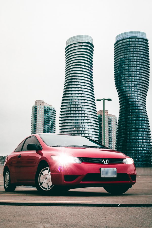 A red honda civic parked on a pavement next to some tall buildings.
