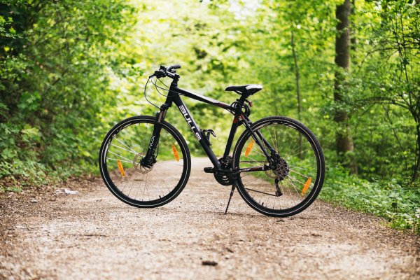 A black mountain bike parked on a dirt road with trees on either side of the road.