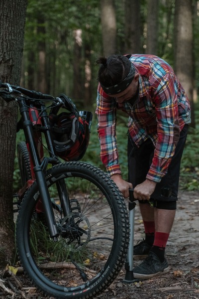 A man outdoors in the woods pumping air into his bike tire.