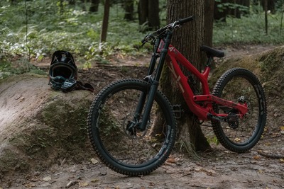 A red downhill mountain bike on a dirt road is parked by a tree.